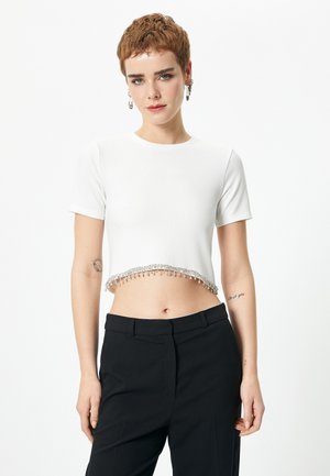 Hvid cropped t-shirt med korte ærmer, med en perlekant. Kombineret med sorte højtaljede bukser. Glat tekstur.