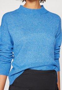 Blauer gestrickter Pullover mit geripptem Rundhalsausschnitt und langen Ärmeln; verfügt über ein strukturiertes Muster und seitliche Schlitze am unteren Saum.