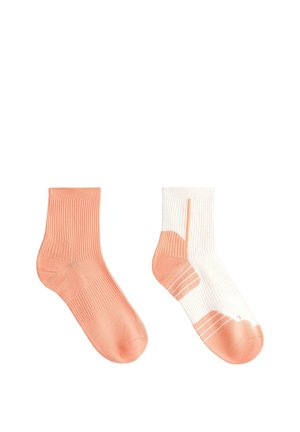 Dve členkové ponožky, jedna jednofarebná broskyňová a druhá biela s broskyňovým pätným dielom, špičkou a pruhmi na bielom pozadí.