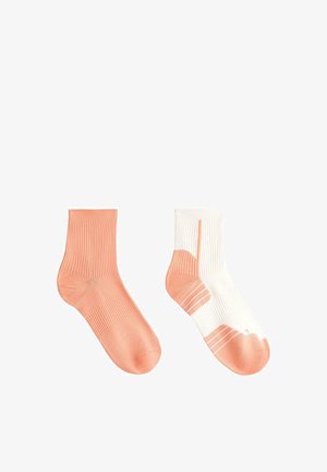 Dve gležnjarici, ena enobarvna breskova in ena bela z breskovim peto, prsti in črtami na belem ozadju.