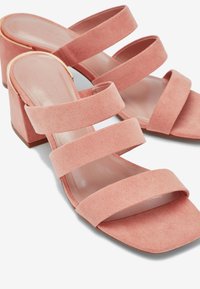 Sandales en suede rose à talons bloc, présentant trois larges brides sur le pied et un design à bout carré, avec une doublure intérieure lisse.