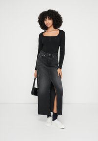 Zwarte lange denim rok met een zij-split, voorzien van zilveren studs langs de linkernaad. Gecombineerd met een zwarte lange mouwen top en witte sneakers.