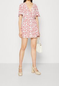 Bloemen wikkeljurk met korte mouwen in rood en wit. Gecombineerd met een witte handtas en beige blokhak schoenen. Soepele stof.