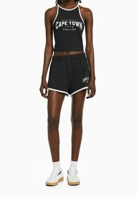 Svart kort topp med vit kant, med texten "CAPE TOWN". Svarta shorts med vita detaljer och tryckt logotyp. Kombinera med vita sneakers.