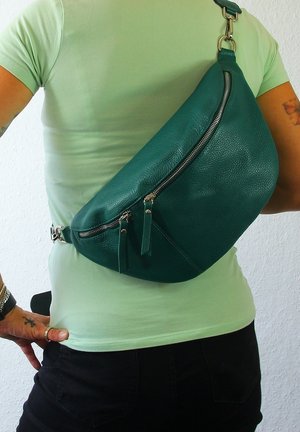 Teal leren sling bag met een gebogen ontwerp, met een ritszak en franjes. Over de schouder gedragen, met metalen hardware.