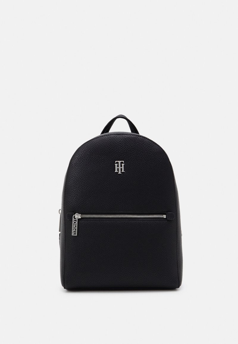Sac à dos en cuir noir texturé avec une poche avant zippée et un petit logo d'initiales argentées près du centre supérieur.
