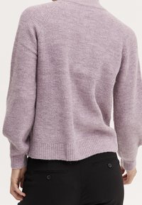 Fialový pletený svetr s ribbovanou texturou, zkráceným spodním lemem a dlouhými rukávy, nošený přes černé kalhoty. Má vysoký výstřih a měkký materiál.
