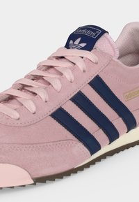 Ροζ αθλητικό παπούτσι Adidas με ναυτικό μπλε ρίγες, ταιριαστά κορδόνια και λαστιχένια σόλα, εμφανιζόμενο σε κοντινή γωνιακή λήψη.