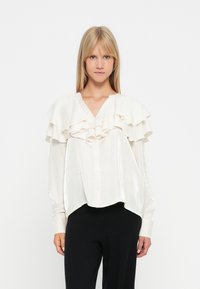 Witte blouse met gelaagde ruches op de schouders, knoopsluiting en lange mouwen; gladde textuur, losse pasvorm en afgeronde zoom.