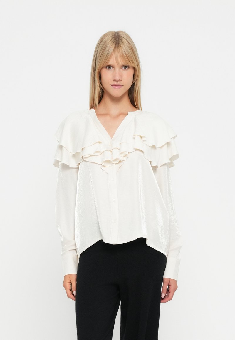 Witte blouse met gelaagde ruches op de schouders, knoopsluiting en lange mouwen; gladde textuur, losse pasvorm en afgeronde zoom.