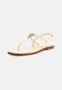 Beiga platta sandaler med T-remdesign, utrustade med en dekorativ metallaccent och en slät läderliknande yta. Klassisk, minimalistisk estetik.