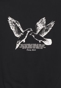 T-shirt nera con grafica bianca di due piccioni con piume dettagliate e testo accompagnatorio in un carattere a contrasto.