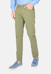 Chino slim-fit verde oliva con chiusura a bottone e tasche laterali, abbinati a scarpe slip-on blu. Camicia di jeans con pois blu.