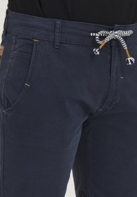Pantalone u mornarsko plavoj boji od mješavine pamuka, s elastičnom fasetom i crno-bijelim kariranim uzorkom, te žutim šavovima na džepovima.
