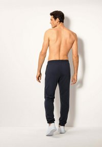 Dunkelblaue Sweatpants mit elastischem Bund und Bündchen, aus weichem Material. Das Modell wird von hinten gezeigt und trägt weiße Sportschuhe.