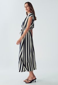 Raitapaituli maxi-mekko tummansinisestä ja krémistä, jossa on vyötärön kireys, lyhyet hihat ja ilmava muotoilu, yhdistettynä mustiin korkokenkiin.