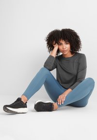 Long-sleeve dark gray top, light blue leggings with side seams, and black athletic shoes. Sitting pose on a plain white background.
