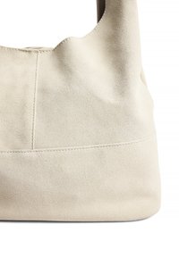 Krämfärgad mockaväska med en mjuk textur, avslappnad design och enkel sömnad längs botten för extra detalj.