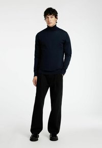 Mornarsko modra turtleneck pulover iz mehkega materiala, v kombinaciji z črnimi širokimi hlačami in črnimi čevlji, z gladko površino brez vzorcev.