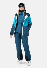 Vinter ski outfit i marineblå og turkis med en softshell-jakke, termisk inderlag og matchende bukser. Har hætte og handsker.