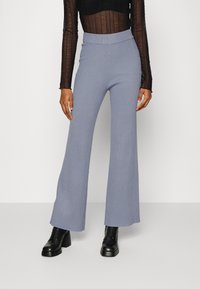 Ljusblå ruggad vida byxor med hög midja, kompletterat med en svart spetsblus med lång ärm och kraftiga svarta stövlar.