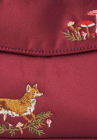 Borsa satinata bordeaux con un ricamo di volpe e funghi. Presenta cuciture intricate e una superficie liscia e lucida.