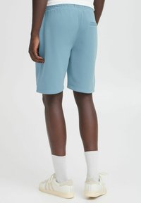 Shorts din bumbac bleu deschis cu talie elastică, având un singur buzunar pe spate și o croială lejeră. Asortați cu șosete sportive albe și pantofi.