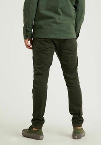 Olijfgroene joggers met elastische manchetten, twee achterzakken en een gladde, duurzame stof. Gecombineerd met bijpassende groene schoenen.
