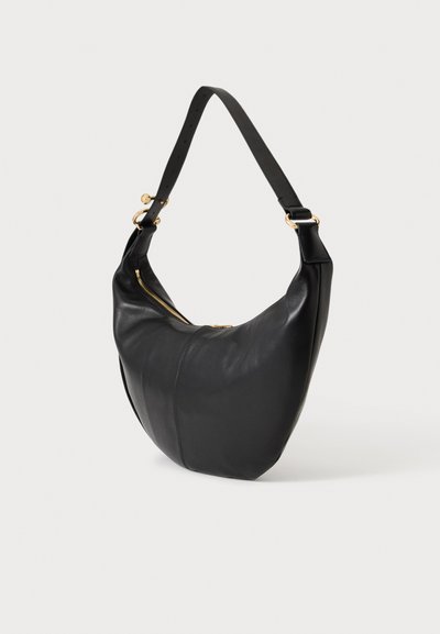 Sac à bandoulière en cuir noir avec une sangle large réglable et un détail de fermeture éclair dorée sur fond uni clair.