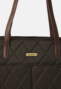 Donkergroene gewatteerde stoffen tas met bruin leren handvatten en een klein gouden Barbour-logo label op de voorkant.