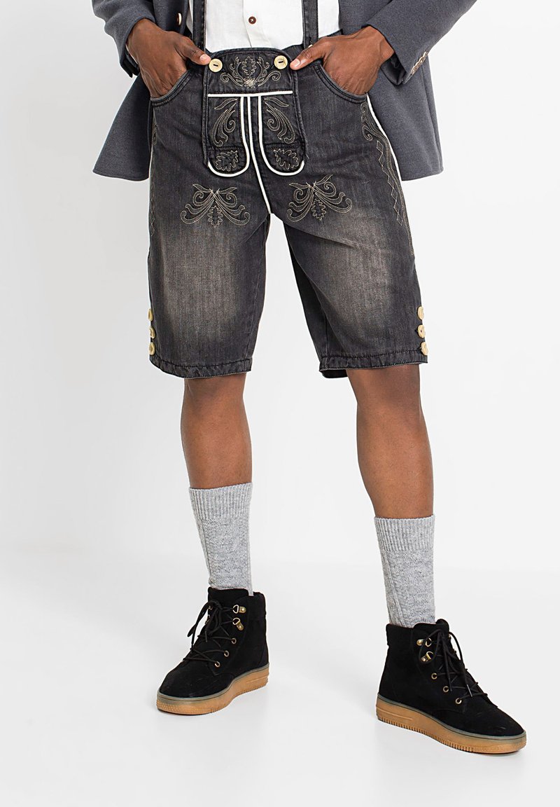 Pantaloni corti in denim lederhosen, grigi scuri con dettagli in ricamo dorato, tasche, bottoni laterali, abbinati a calzini a maglia grigi e stivali neri.