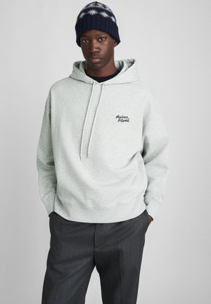 Sweat à capuche gris clair avec cordons de serrage et logo brodé sur la poitrine gauche, associé à un pantalon habillé gris foncé et à un bonnet en tricot à motifs bleu marine.