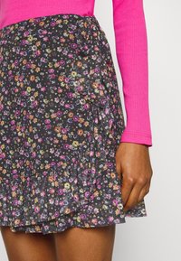 Sort blomsterkjole med bølgende kant, pyntet med flerfarvede blomster. Bånd i taljen og letvægtsstof, parret med en lyserød langærmet top.