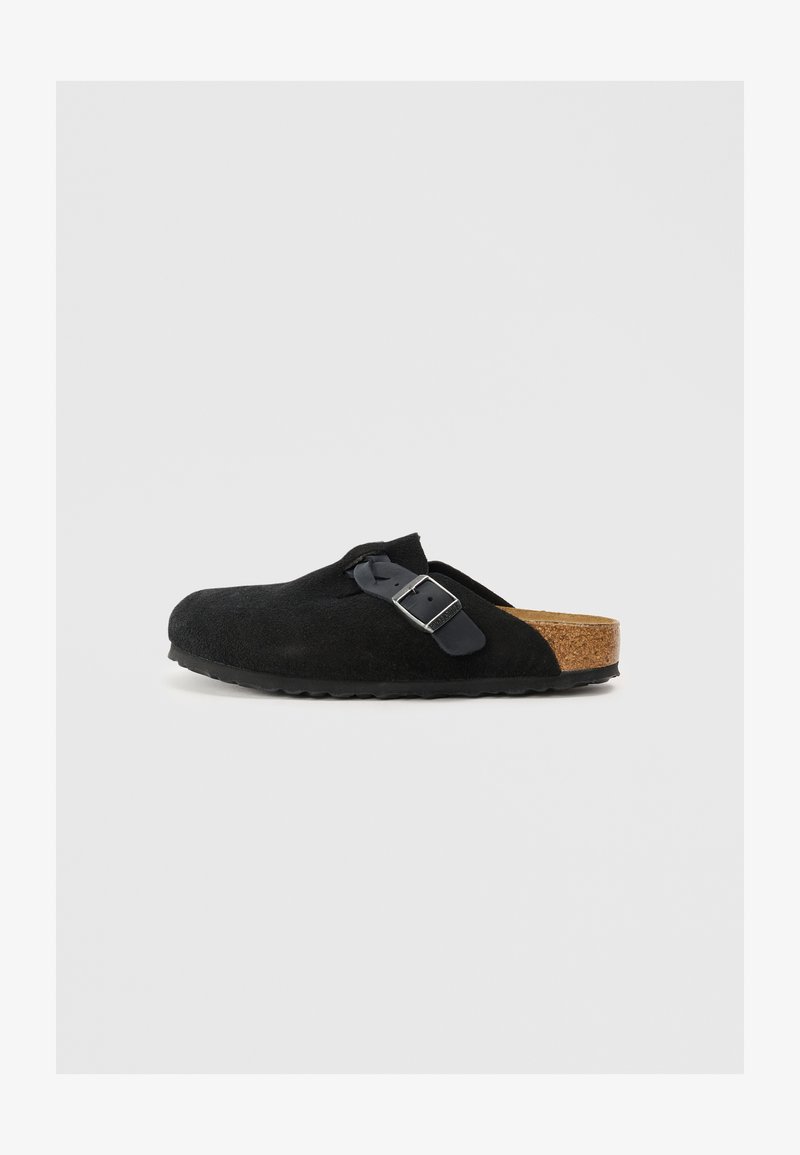 Black suede slip-on shoe with a cork sole, featuring a side buckle detail and a rounded toe design. Flat, textured rubber outsole.