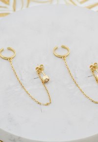 Guldtonade örhängen med en hoop-design kopplad av en kort kedja till en cylindrisk stav med en klar stenaccent.