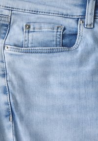 Jasnoniebieskie dżinsy z tylną kieszenią z metalowym guzikiem, delikatnym wyblaknięciem i diagonalną fakturą splotu.