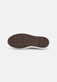 Semelle d'une basket blanche Converse montrant une bande de roulement en caoutchouc marron avec des motifs en losange et des lignes sur un fond blanc uni.