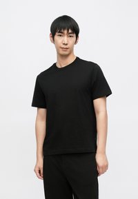 Černé bavlněné tričko s krátkými rukávy, kulatým výstřihem a volnějším střihem. Hladká textura bez viditelných vzorů nebo zdobení.