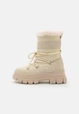 Beige ankle boots with a fluffy cuff, suede and textile upper, front lacing with metal hooks, and thick, rugged sole.