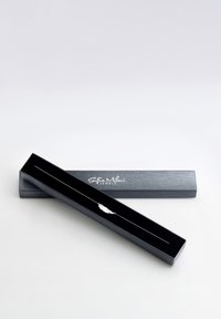 Svart smyckeskrin med ett silverfjäderhänge inuti, som visar en elegant design och slät yta, prydd med fina kedjelänkar.