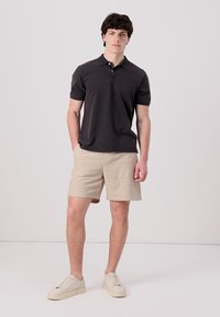 Mørkegrå polo med korte ermer, beige linses shorts og beige joggesko, som gir en uformell og avslappet stil.