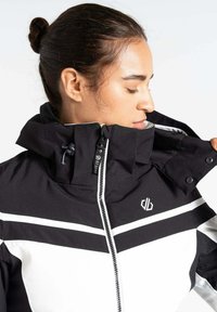 Schwarz-weiße isolierte Jacke mit hohem Kragen, Reißverschluss vorne und Logos. Verfügt über auffällige weiße Streifen und eine strukturierte Oberfläche.