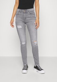 Jeans de denim cinza com um corte slim, apresentando detalhes rasgados, um leve desbotamento e uma cintura de altura média. Combinados com ténis pretos.
