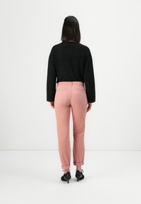 Svart texturerad tröja med långa ärmar, kombinerad med ljusrosa tapered-byxor och svarta klackskor, sett bakifrån.