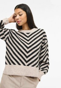 Pull rayé noir et crème avec un motif chevron, une texture douce et un col rond, avec un ourlet légèrement raccourci.