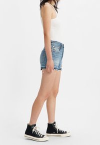 Ljusblå denimshorts med fransad nederkant, tillsammans med en vit tank top och svarta högklackade sneakers. Allt i en avslappnad stil.