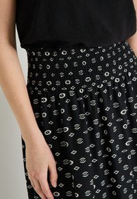 Falda negra con cintura fruncida que presenta un patrón geométrico blanco de diamantes y círculos, confeccionada en una tela ligera.