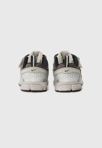 Nike-Schuhe in Grau und Schwarz mit Mesh-Material, geometrischen silbernen Akzenten, gepolstertem Kragen und verstellbarem Riemen. Die Rückansicht zeigt strukturierte Details.