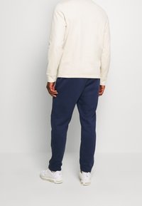 Světle krémová dlouhá košile oblečená s námořnickými tepláky. Doplněno bílými sportovními botami. Hladká látka, volný střih, minimální design.