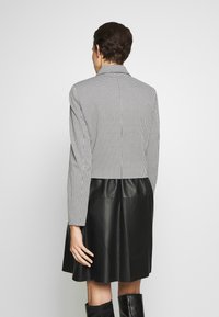 Veste courte à manches longues avec un motif pied-de-poule noir et blanc, col cranté, accompagnée d'une jupe en cuir lisse atteignant la mi-cuisse.